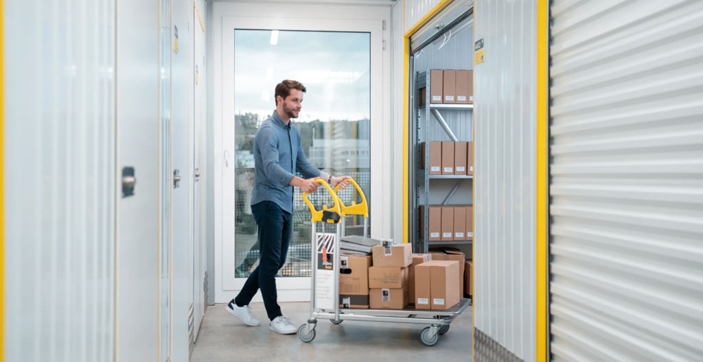 Homme ouvrant la porte métallique de son box de stockage avec un cadenas personnel dans un couloir intérieur bien éclairé d'un centre de self-stockage moderne.